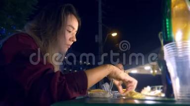 年轻的亚洲女孩晚上在户外<strong>吃街</strong>头食品。